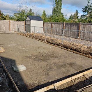 A concrete driveway is being built in a backyard next to a wooden fence.