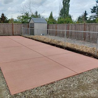 A concrete driveway with a fence and a shed in the background.