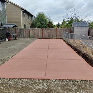 A red concrete driveway in a backyard next to a house and a fence.