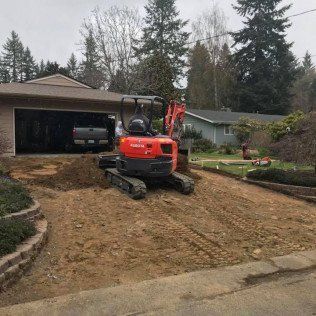 A red excavator is moving dirt in front of a house.