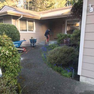 A man is cleaning the sidewalk in front of a house.