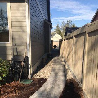 A sidewalk leading to a house next to a wooden fence.