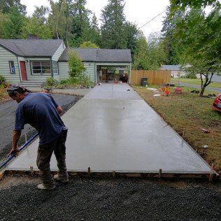 A man is working on a concrete driveway in front of a house.