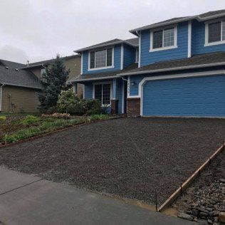 A blue house with a gravel driveway in front of it.