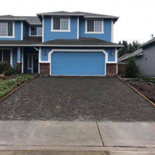 A blue house with a gravel driveway in front of it.