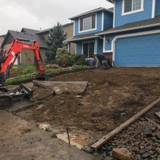 A red excavator is sitting in front of a blue house.