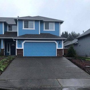 A blue house with a blue garage door and a concrete driveway.