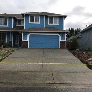 A blue house with a concrete driveway in front of it.