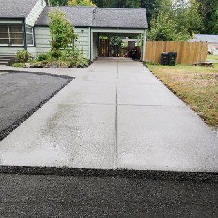 A concrete driveway leading to a house with a wooden fence.