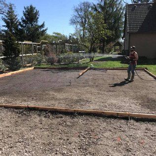 A man is standing in a dirt field in front of a house.