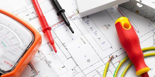 A pair of safety glasses , a screwdriver , and a multimeter are sitting on top of a blueprint.