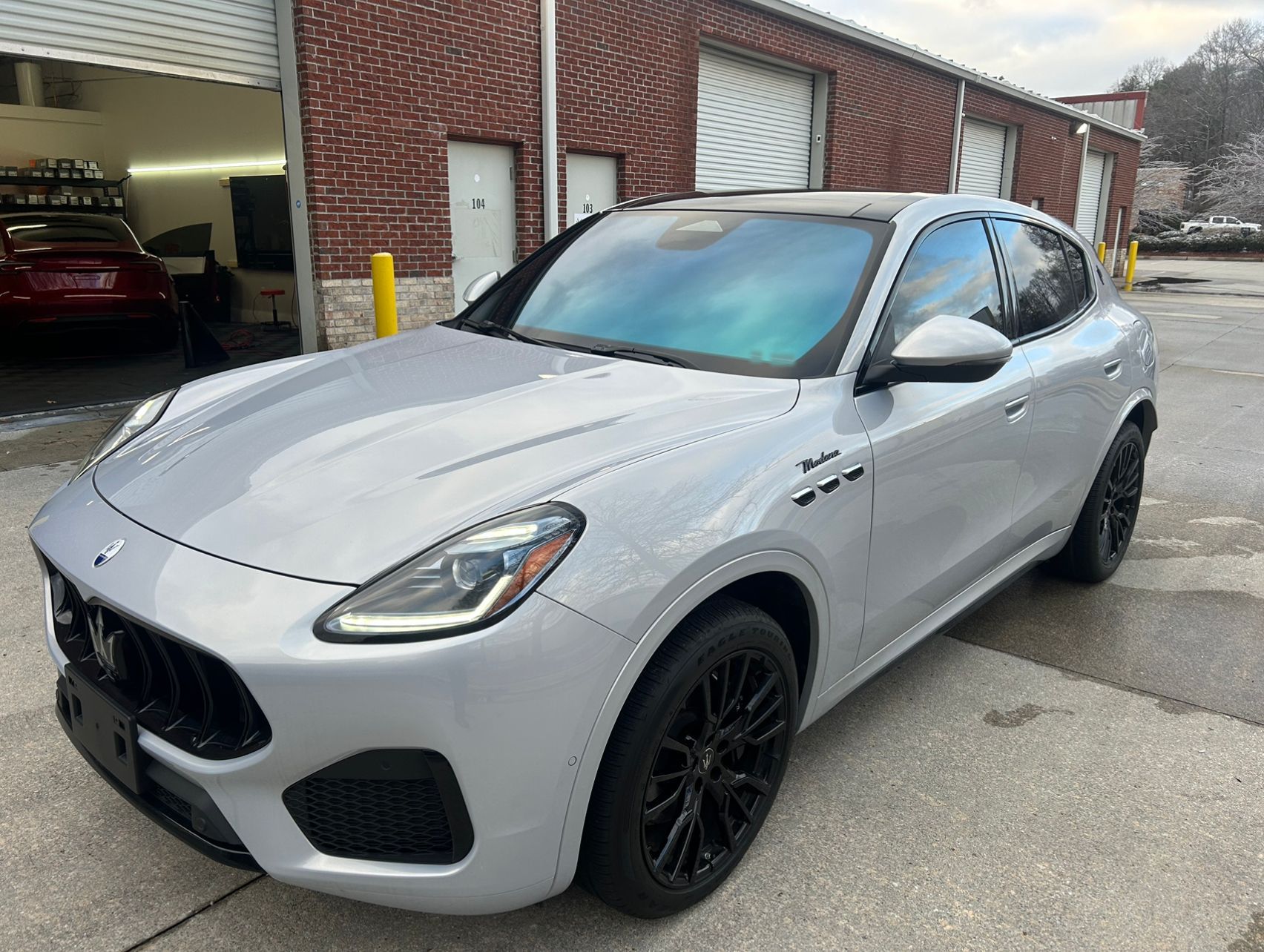 A silver maserati granturismo is parked in front of a brick building.