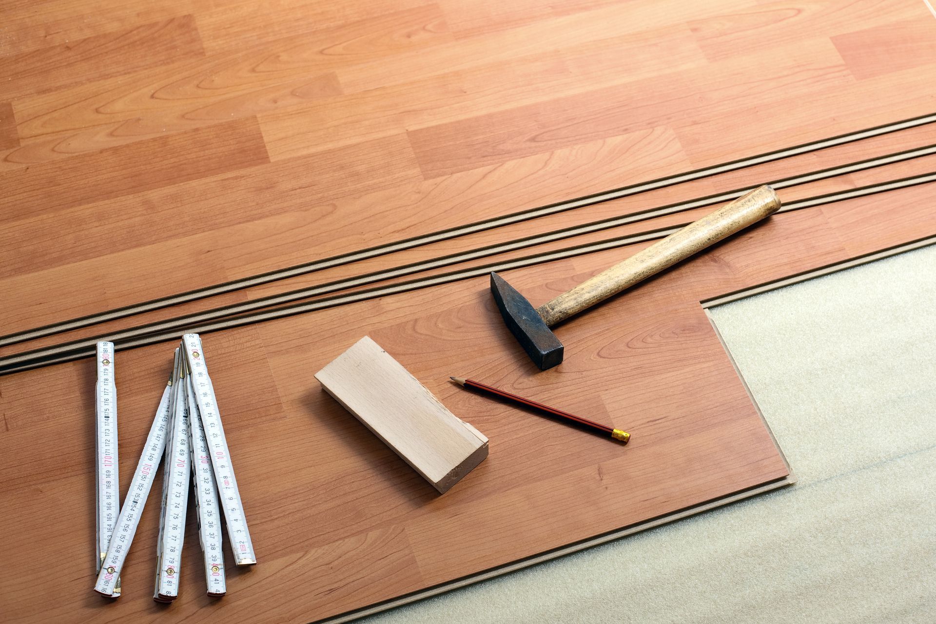 A wooden floor with a hammer , ruler and pencil on it