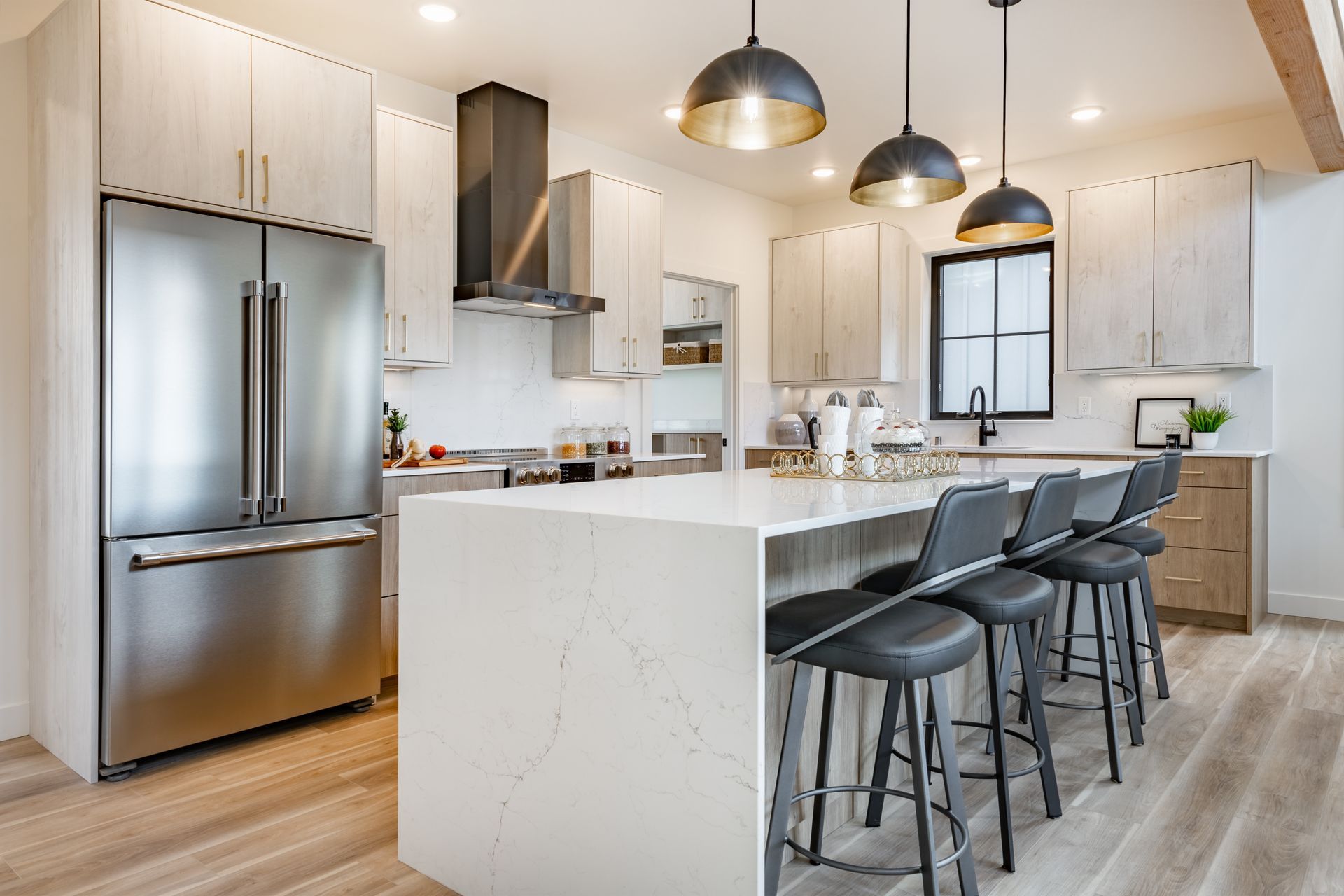 A kitchen with stainless steel appliances , white cabinets , a large island and stools.