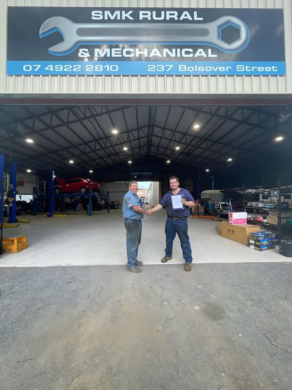 Two Men Are Shaking Hands in Front of a Garage — SMK Rural & Mechanical Pty Ltd in Rockhampton City, QLD