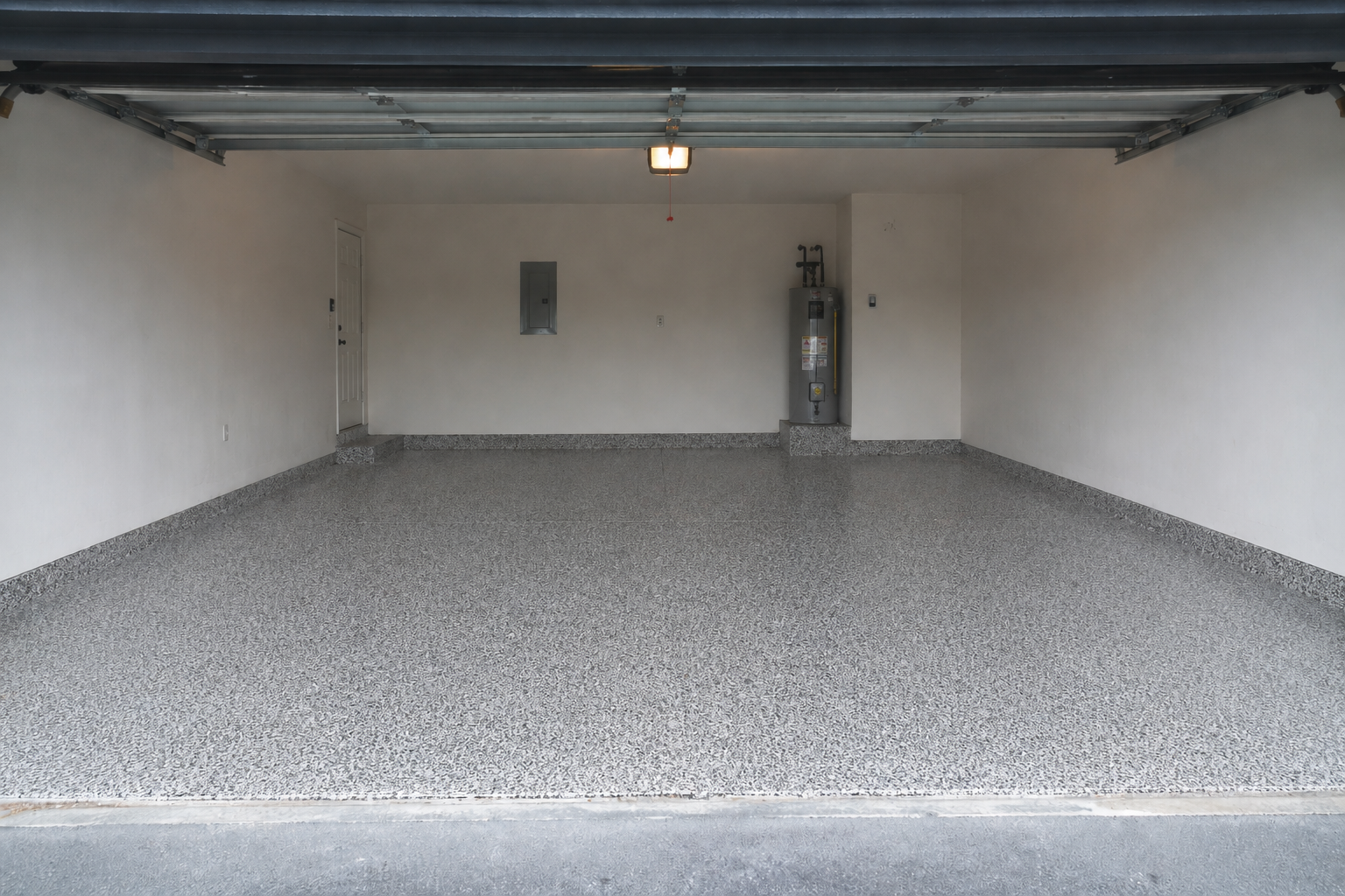 Empty garage with white walls, gray pebble flooring, and an open overhead door.