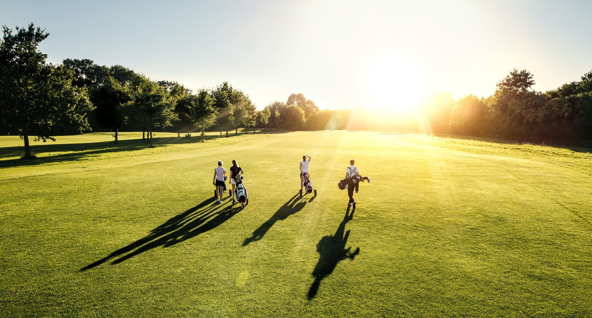 A group of people are walking on a golf course at sunset.