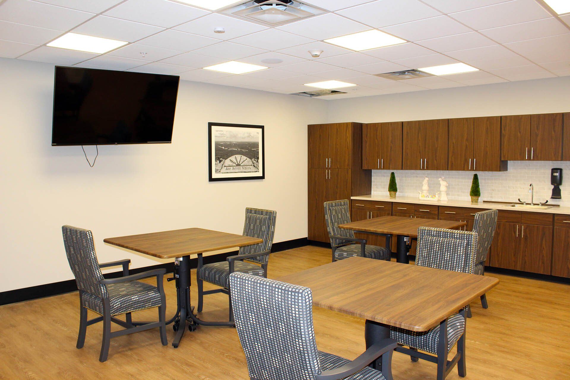 A room with tables and chairs and a flat screen tv on the wall.