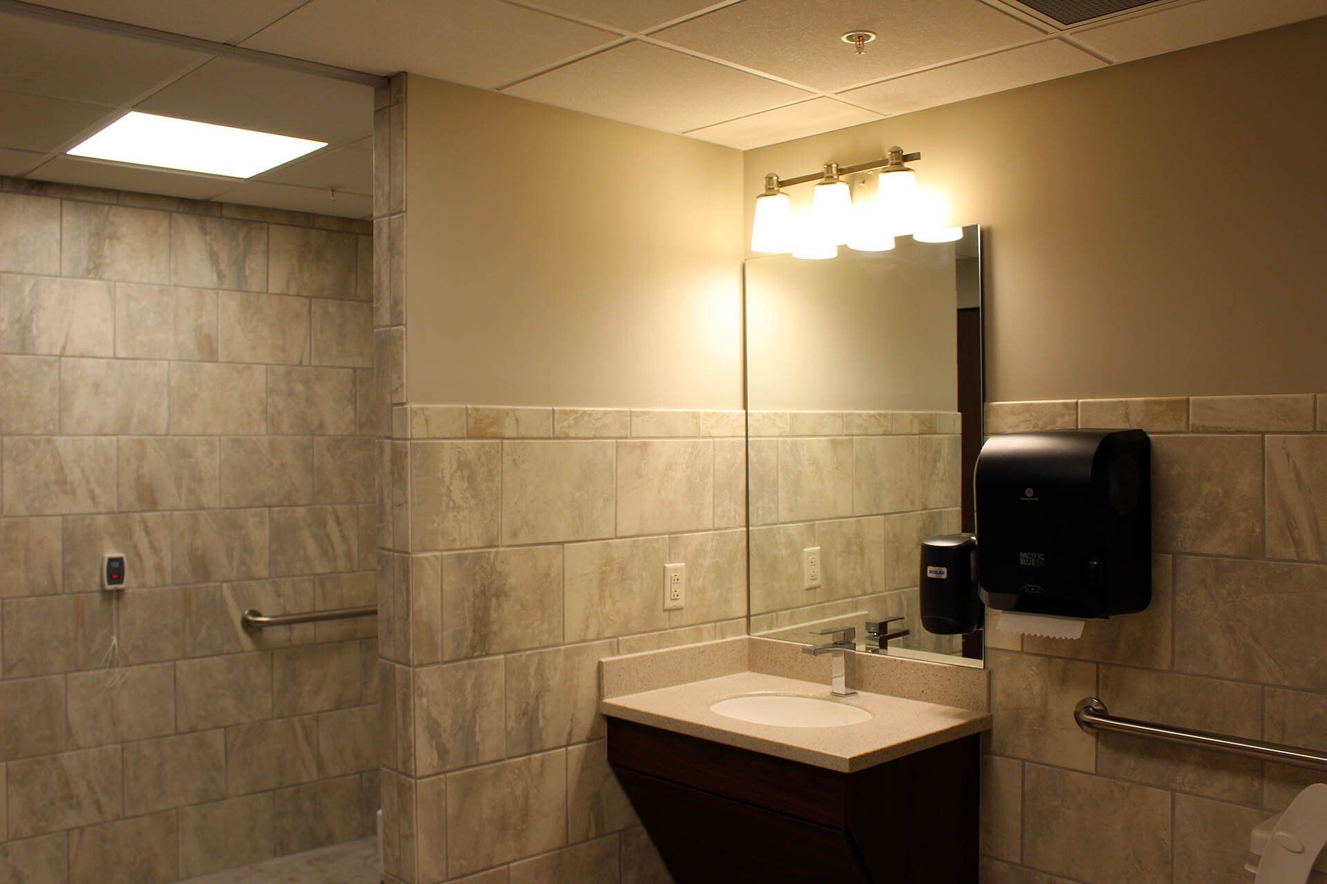 A bathroom with a sink a mirror and a paper towel dispenser