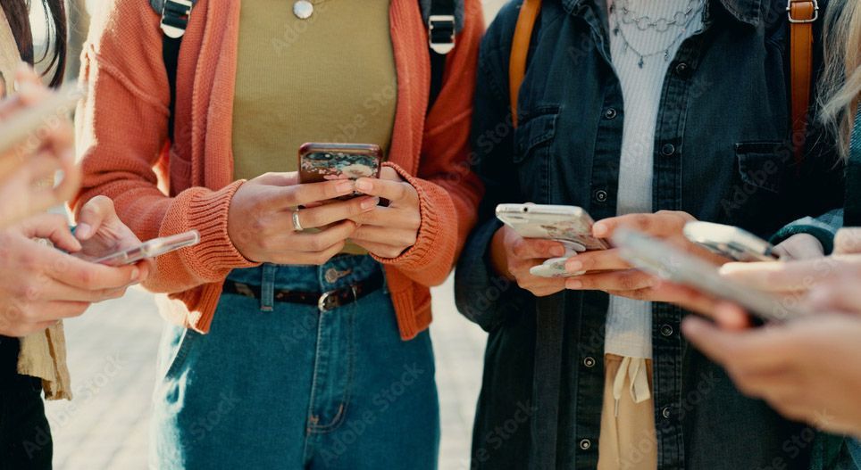 A group of people are standing next to each other looking at their phones.