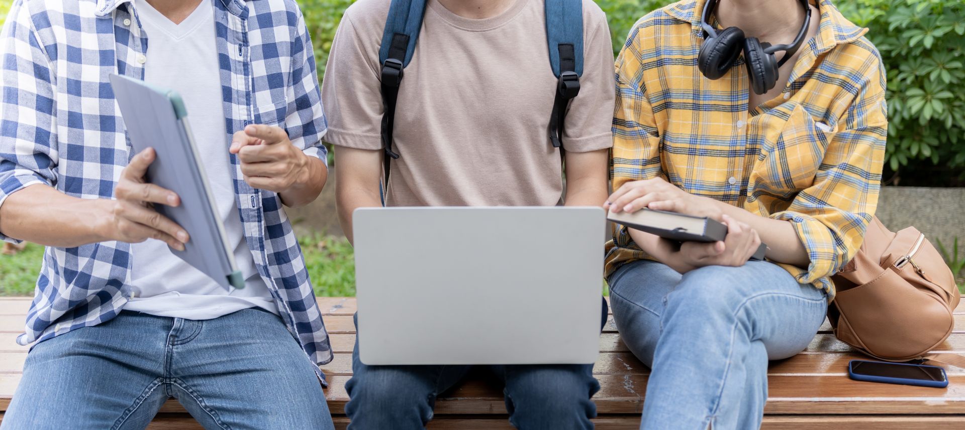 A group of young people are sitting on a bench with a laptop and a tablet.