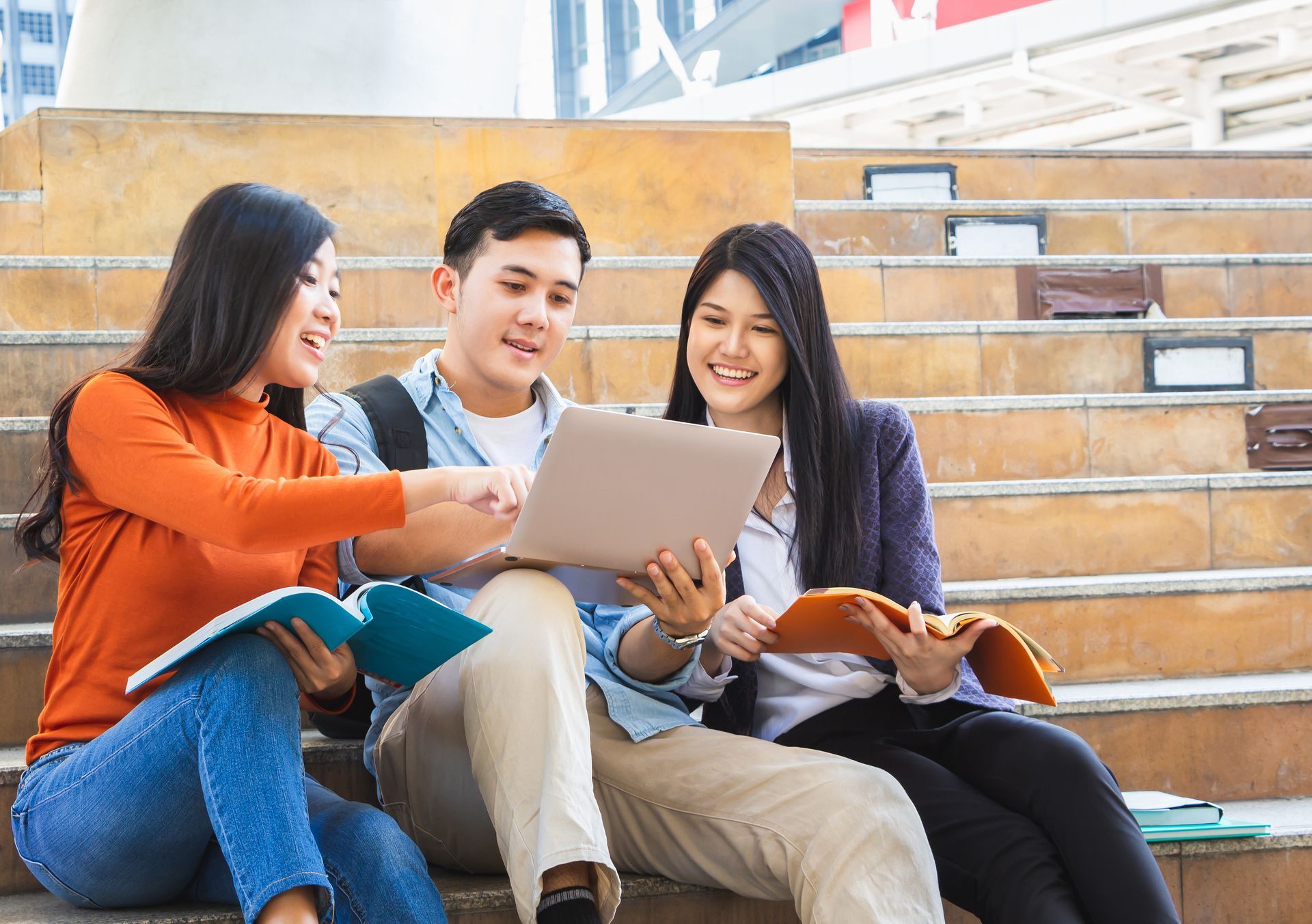 A group of young people are sitting on a set of stairs looking at a laptop.