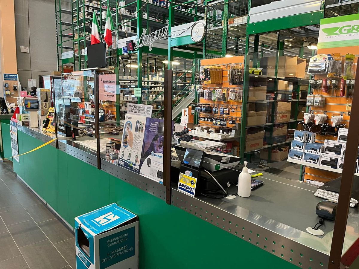 Area bancone in un negozio di ferramenta a tema ecologico con barriere protettive, espositori per i prodotti e bandiera italiana.
