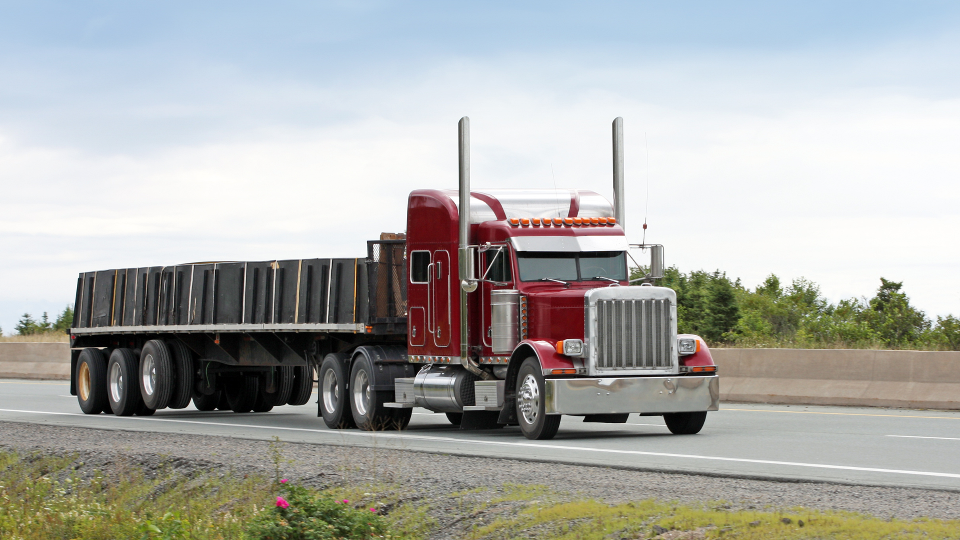 A red semi truck with a flatbed trailer is driving down a highway.