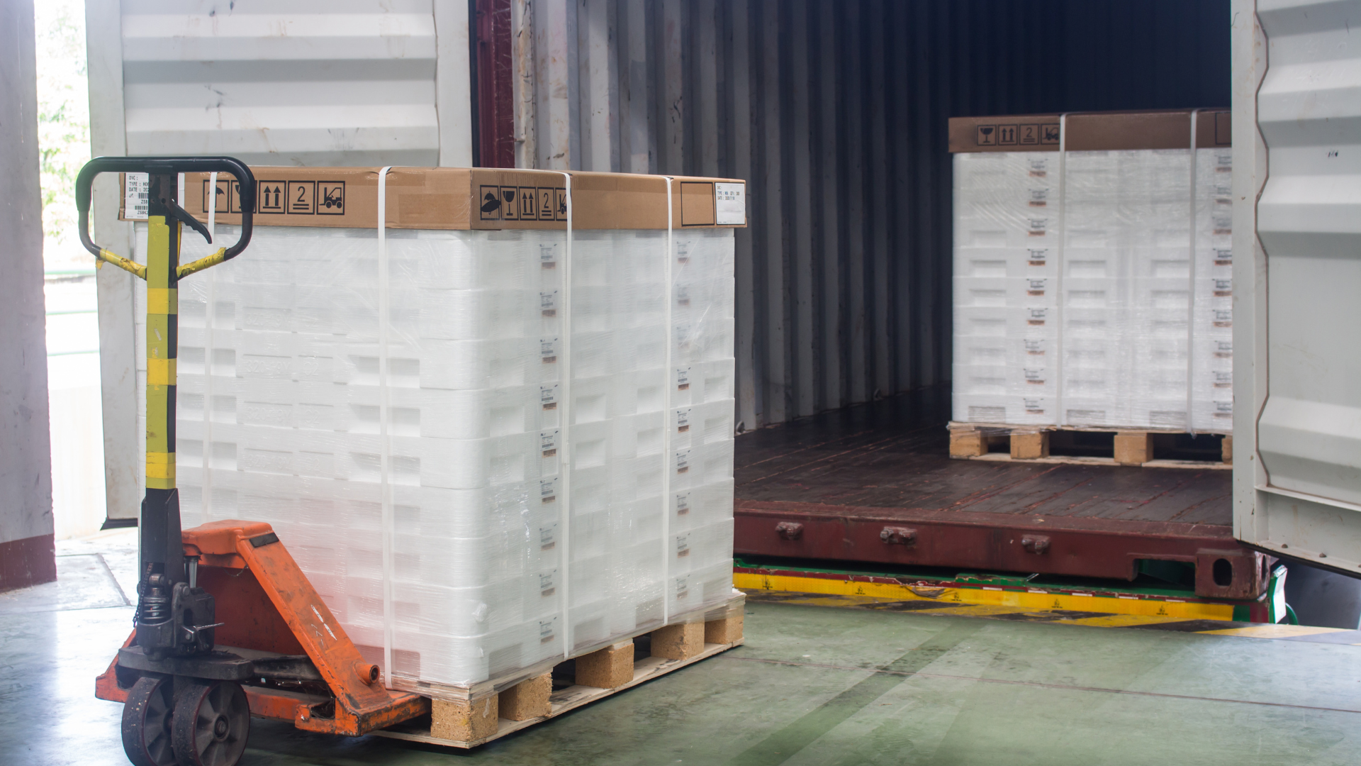 A pallet truck is loading boxes into a shipping container.