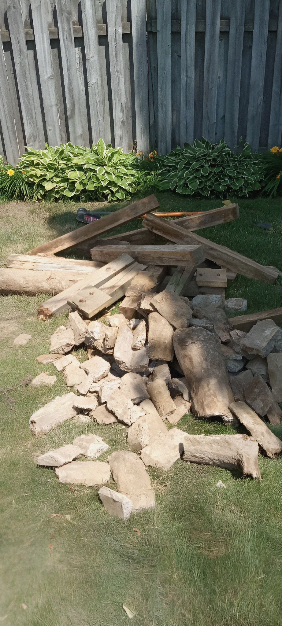 A pile of rocks is sitting on the grass in front of a wooden fence.