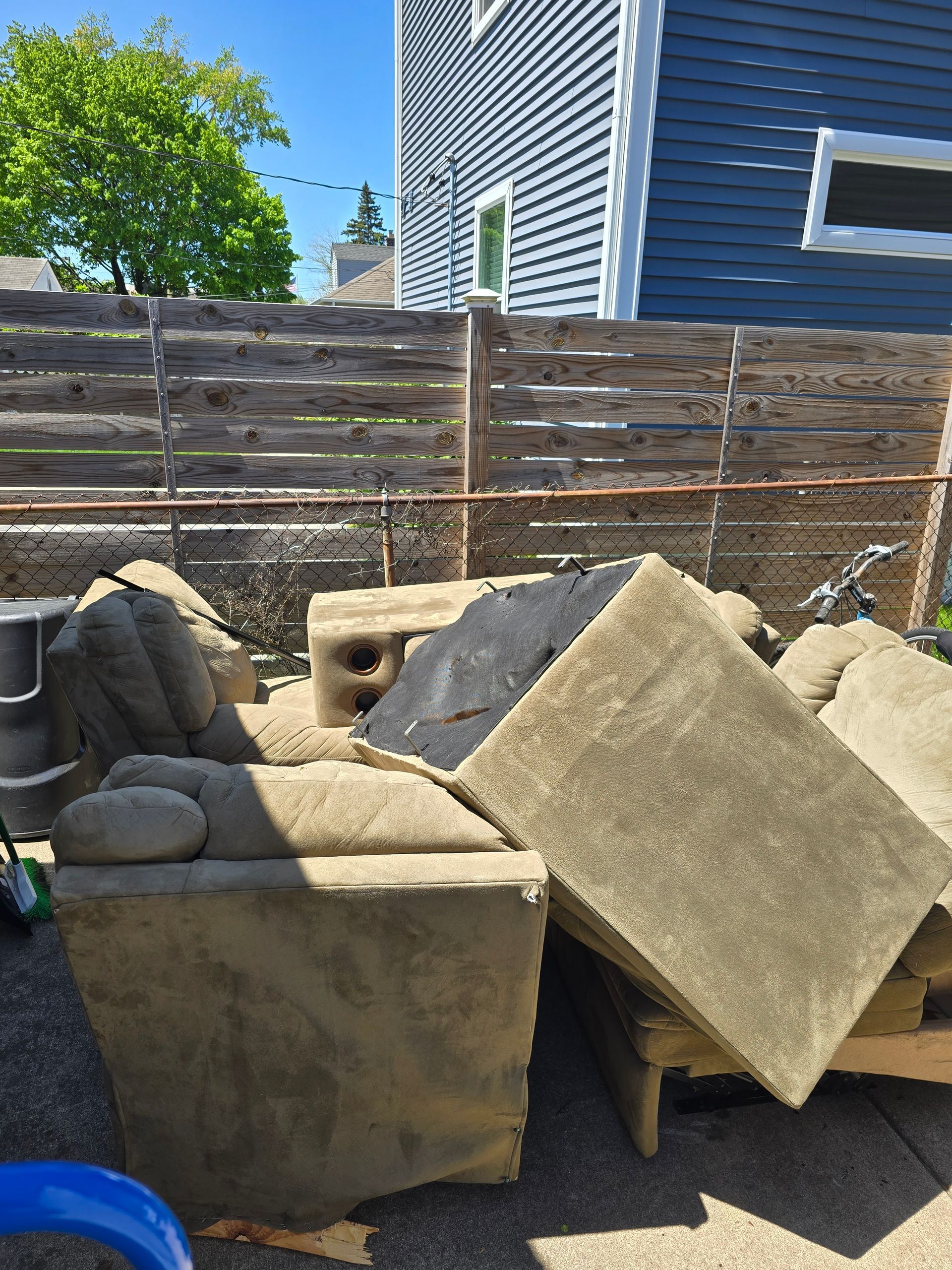 A pile of furniture is sitting on the ground in front of a wooden fence.