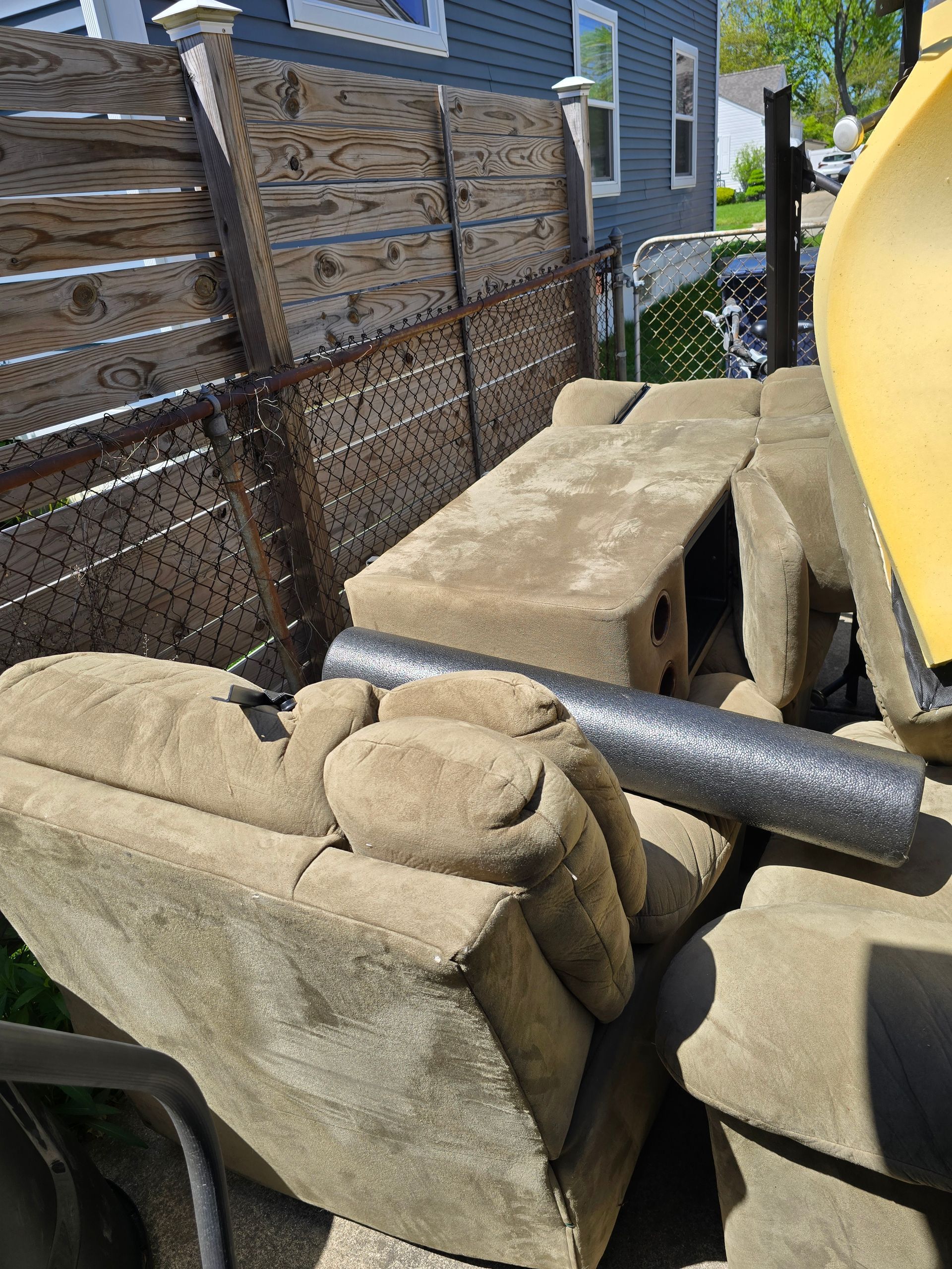 A pile of couch seats is sitting in front of a wooden fence.