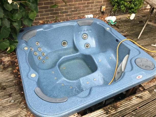 A blue hot tub is sitting on top of a wooden deck and waiting to be removed and hauled away.