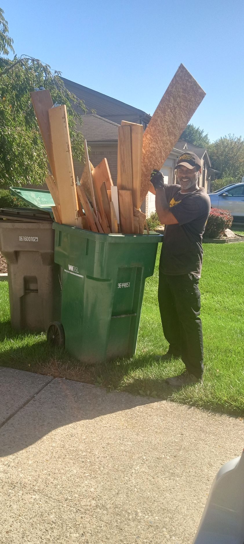 A man is standing next to a trash can filled with wood.