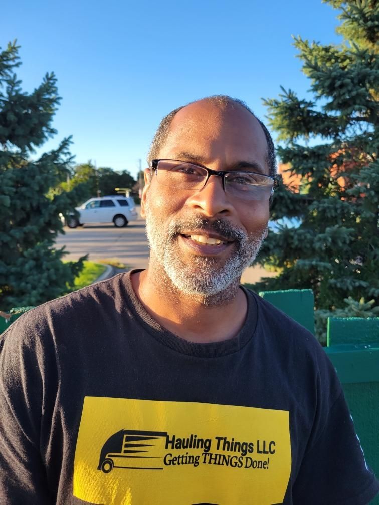 A man wearing glasses and a t-shirt that says hauling things LLC is smiling for the camera.