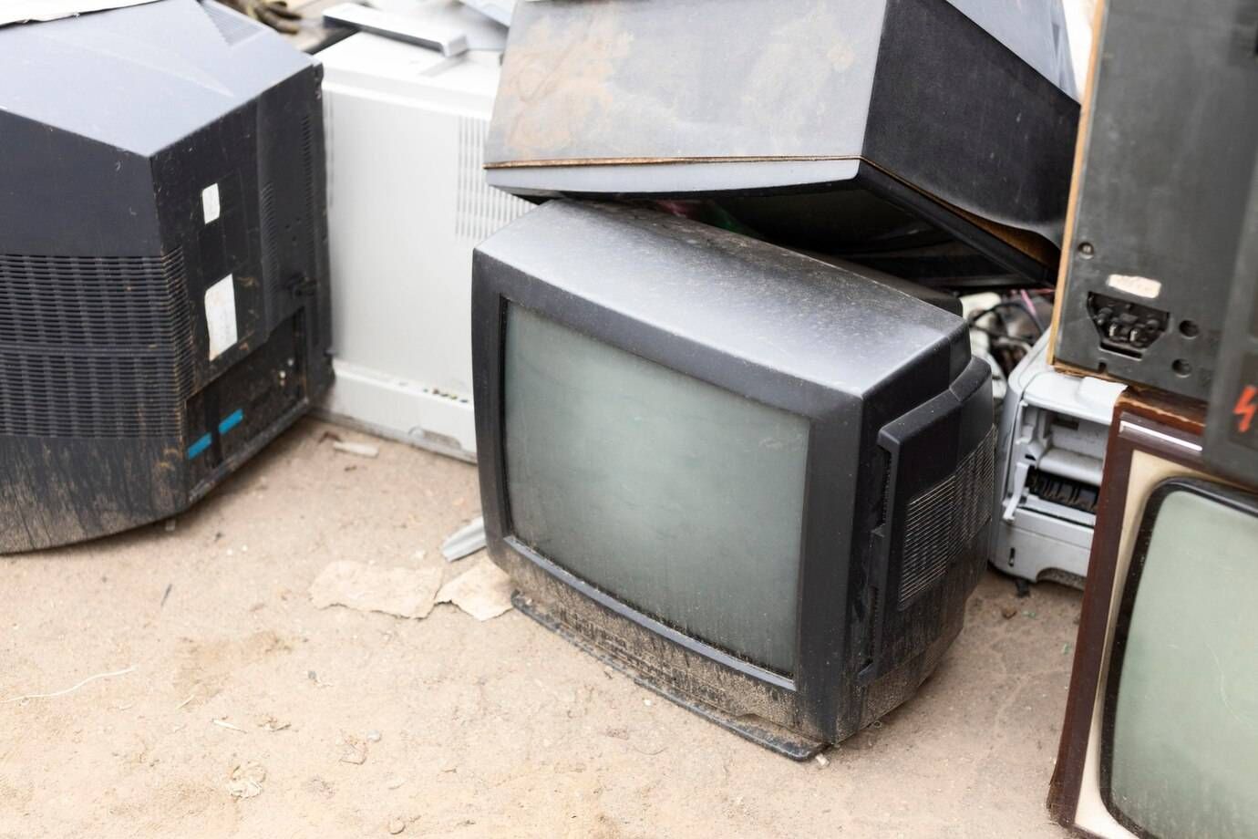 A pile of old televisions are sitting on the ground.