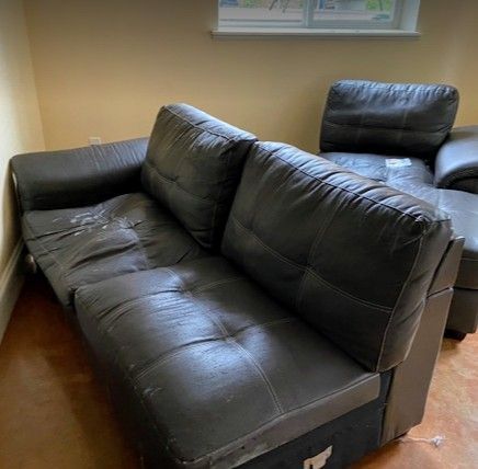 A black leather couch sits in a living room beside a window.