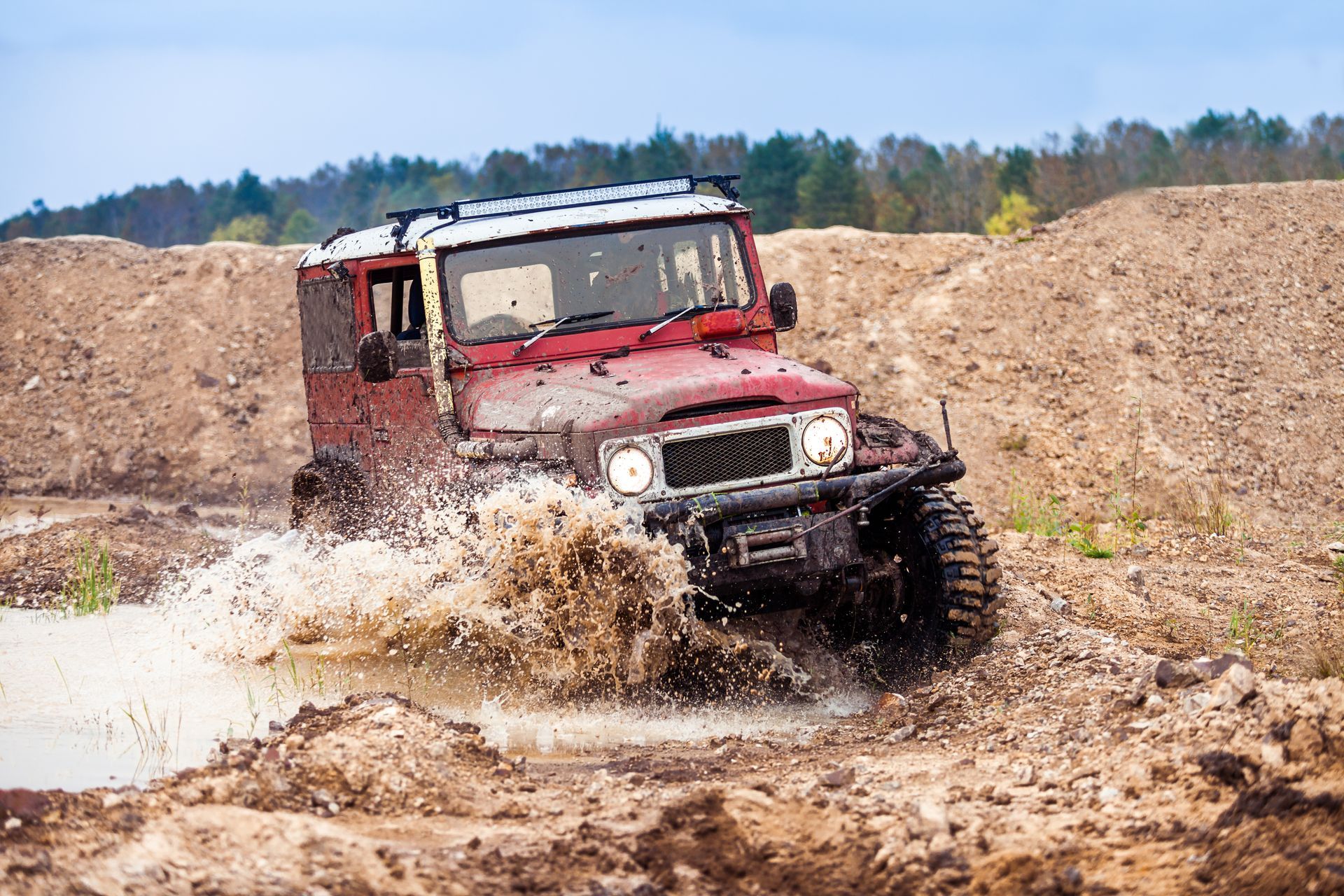 A red jeep is driving through a muddy field.