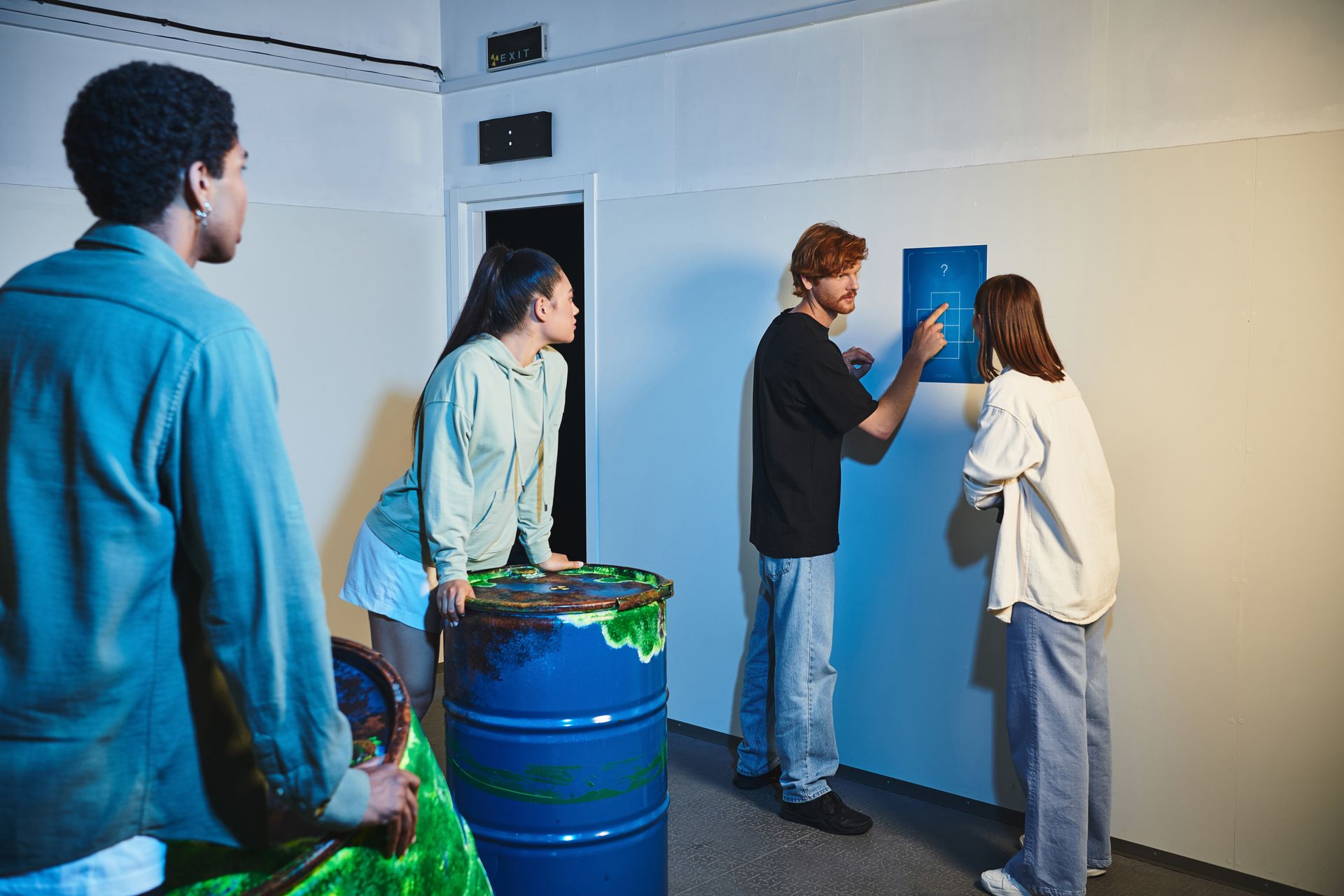 A group of people are standing around a blue barrel in a room.