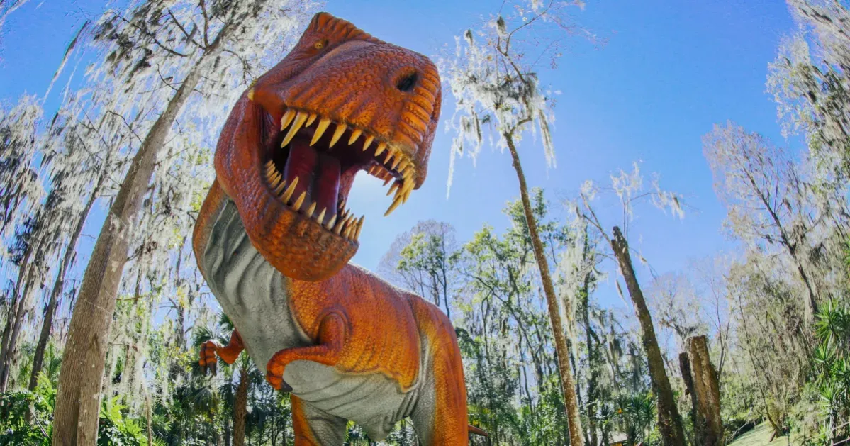 A t-rex statue is standing in the middle of a forest with its mouth open.