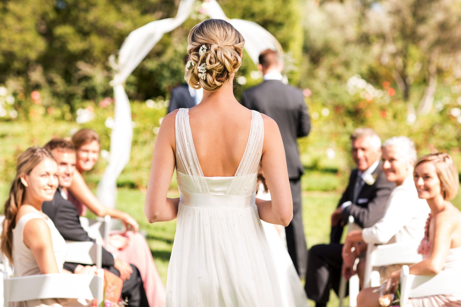 A bride in a wedding dress is standing in front of her wedding guests.