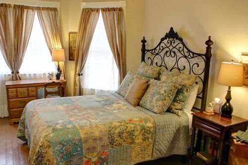 A bedroom with a bed , nightstand , desk and two windows.