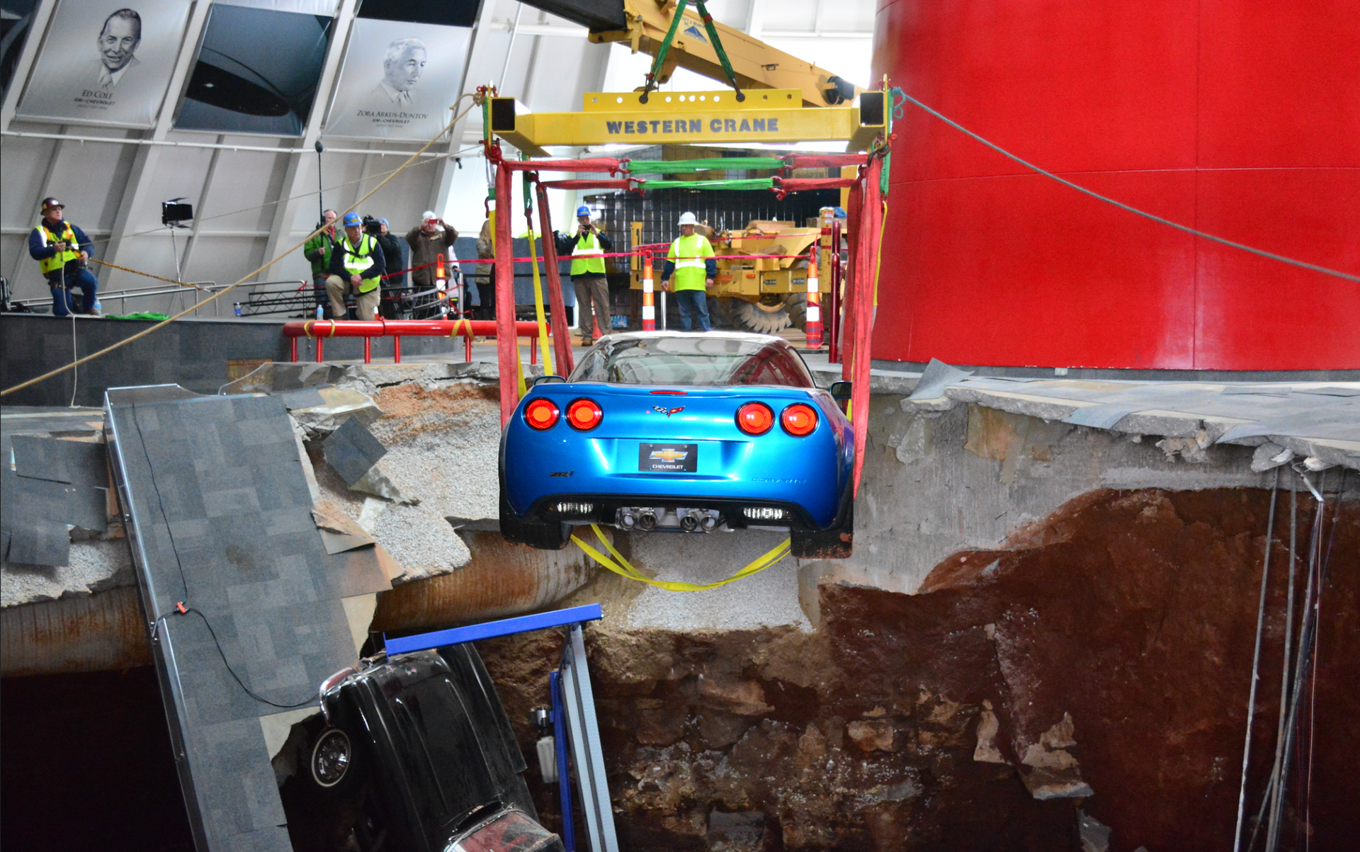 A blue car is being lifted out of a hole in the ground.