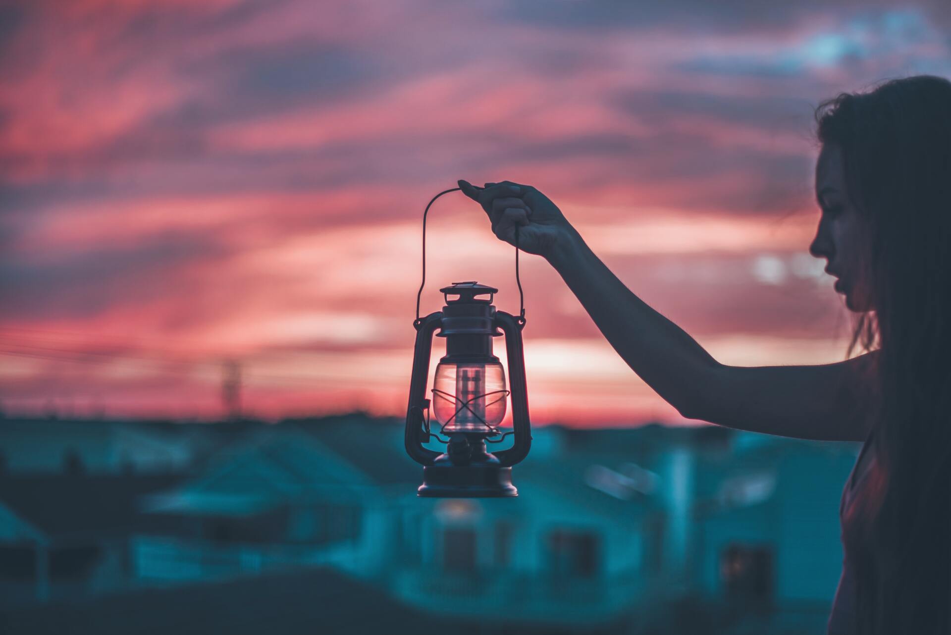 A woman is holding a lantern in front of a sunset.