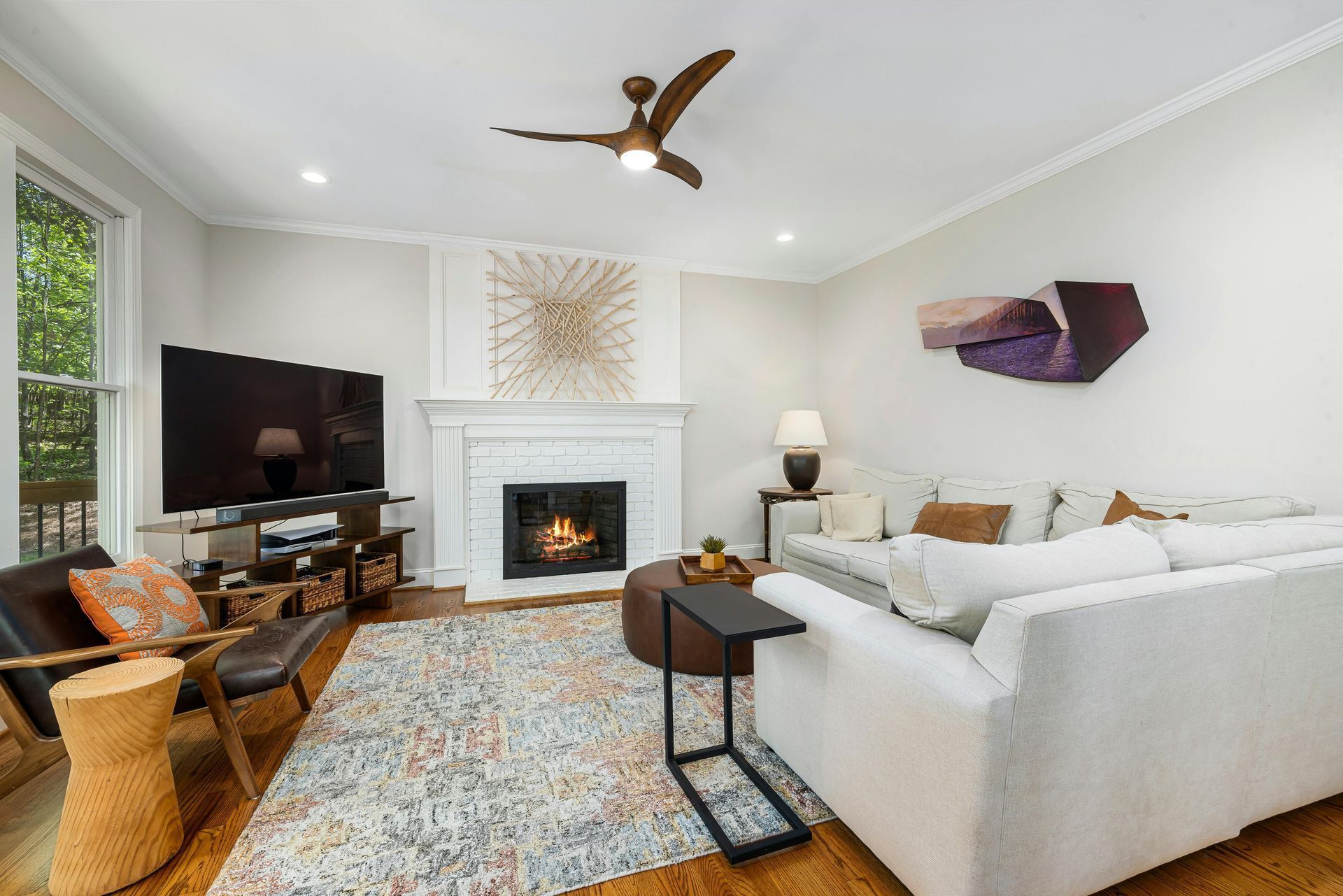 Bright living room with white sofa, fireplace, TV, patterned rug, and large windows