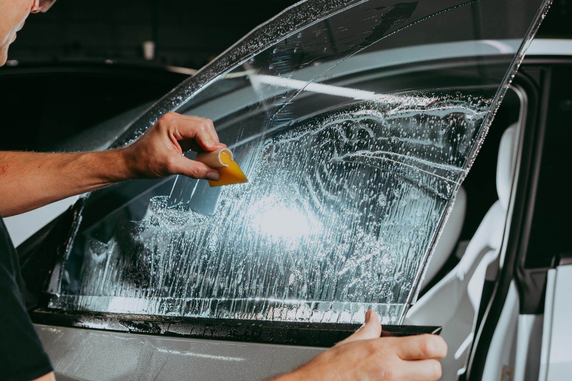 Person scrapes soap off a car window with a yellow squeegee during a car wash