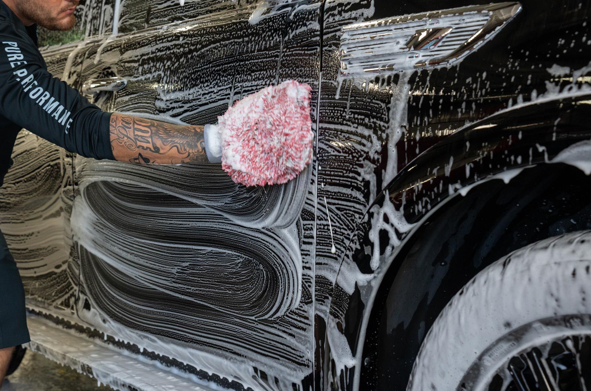 Person washing a black car with pink sponge and white soap suds