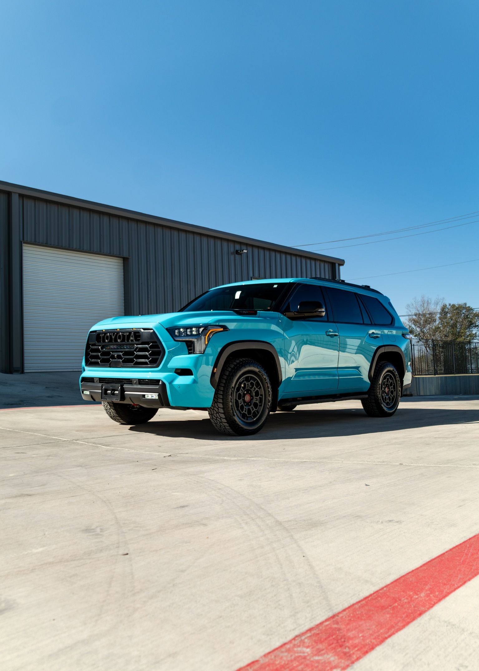 Rear side of a turquoise SUV with black off-road wheel and tire parked in sunlight.