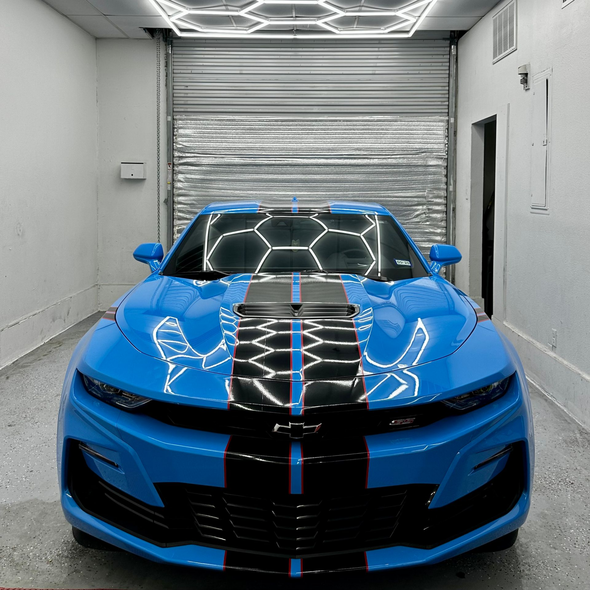 Blue sports car with black racing stripes parked in a garage