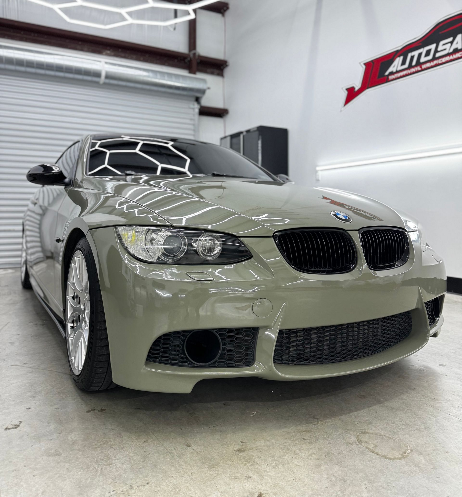 Custom green BMW coupe in a bright auto detailing shop under geometric ceiling lights